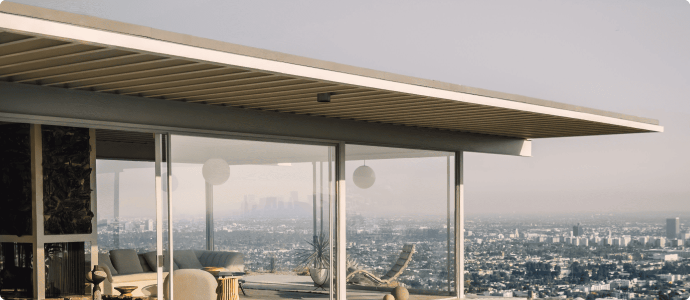 A modern house with large glass panels overlooking a panoramic view of the city during the daytime