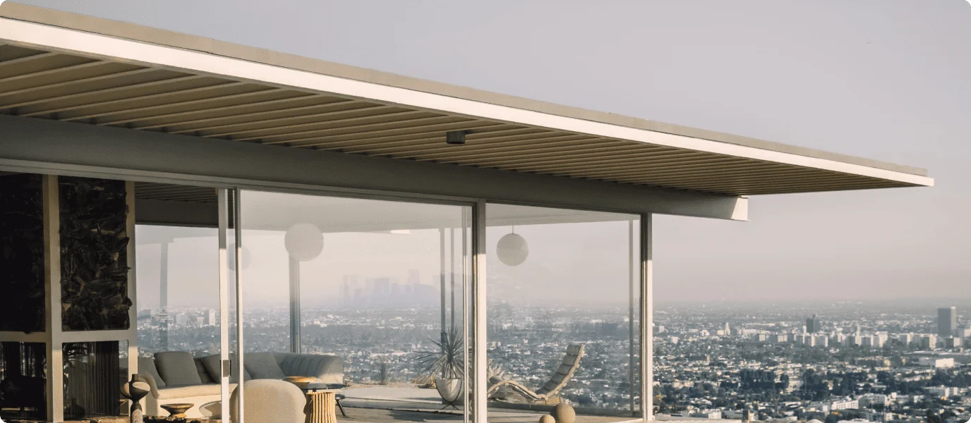 A modern house with large glass panels overlooking a panoramic view of the city during the daytime
