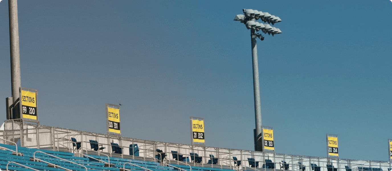 Bleachers of a sports stadium with section number signs and tall floodlights under a clear blue sky