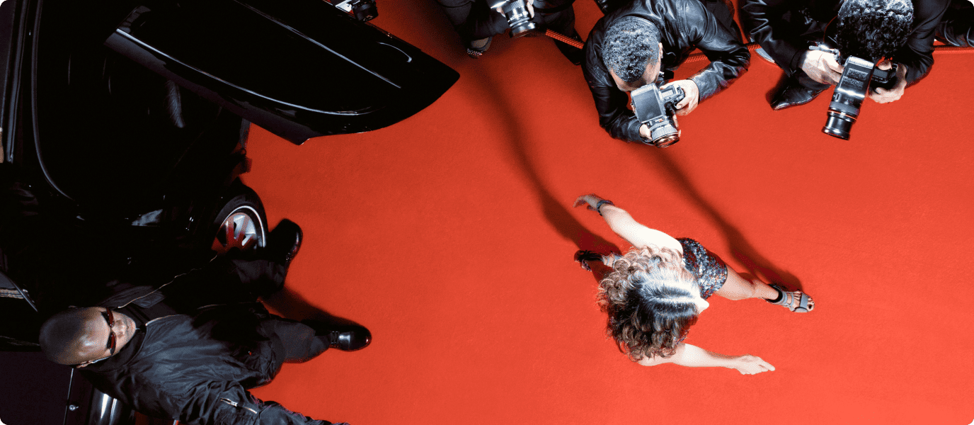 Top-down shot of a person walking on a red carpet, surrounded by photographers and security at an important event.