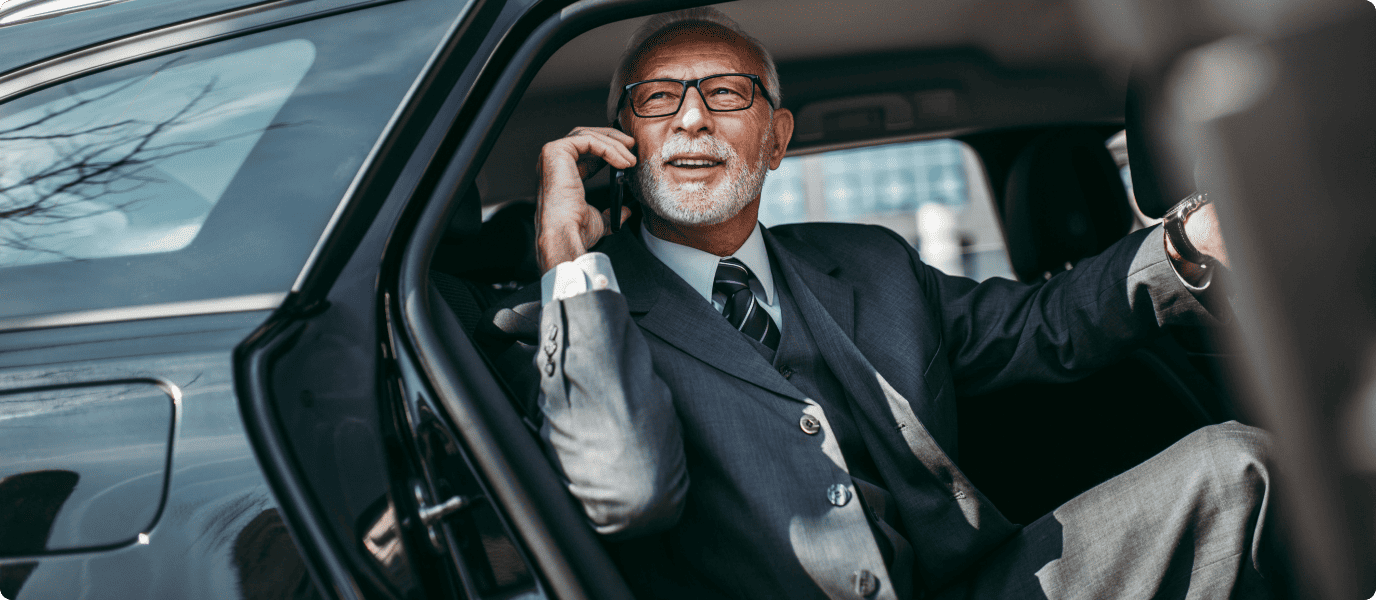 An elegant man in a suit sitting in a luxury car, speaking confidently on his phone