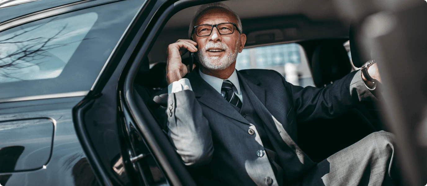 An elegant man in a suit sitting in a luxury car, speaking confidently on his phone